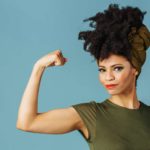 A woman wearing green flexes her bicep.
