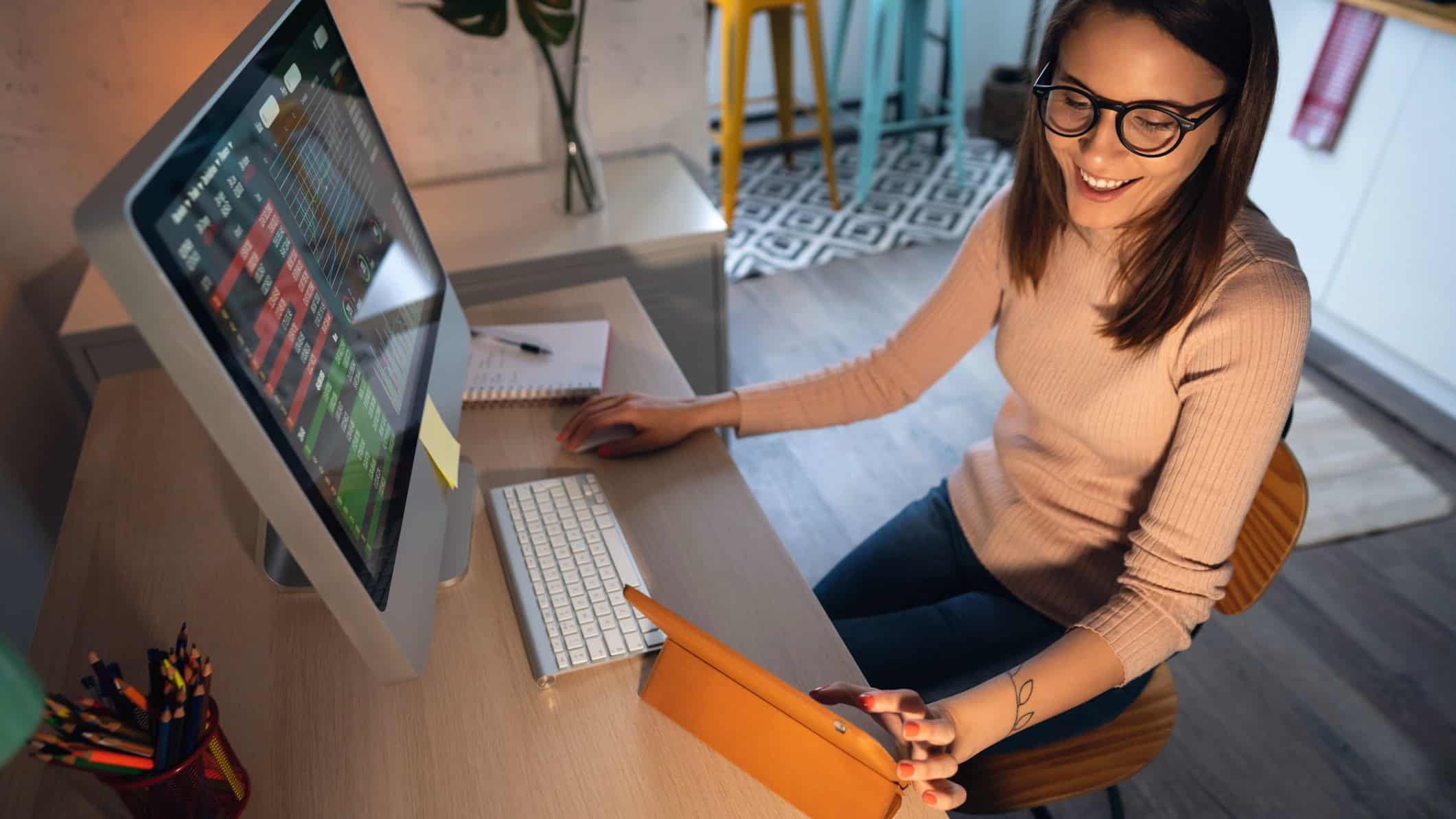 A woman works on her desktop and tablet, having a win with crypto.