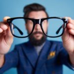 a man wearing a suit holding up his glasses