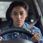 A woman sits miserable behind the wheel of her car.