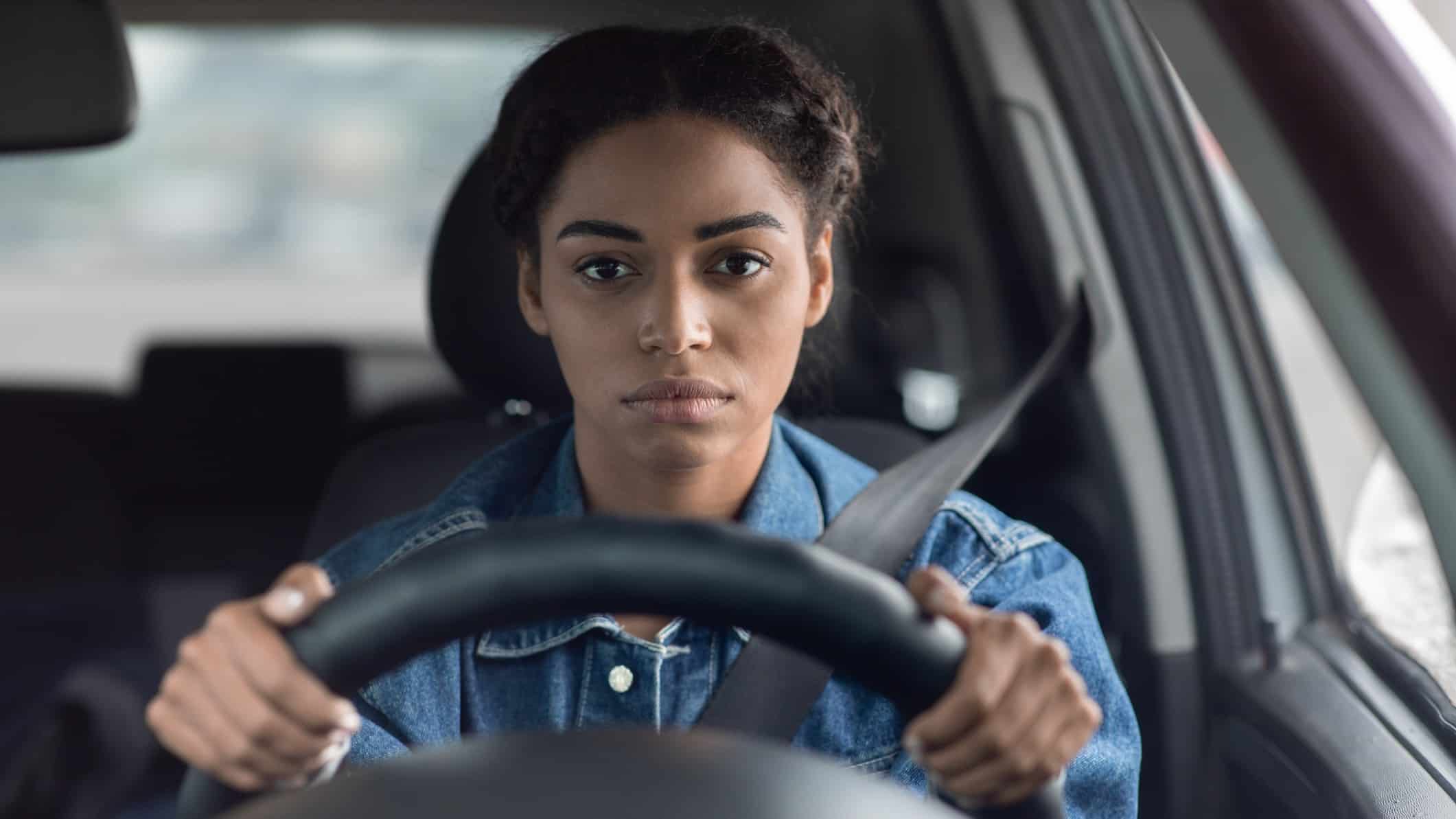 A woman sits miserable behind the wheel of her car.