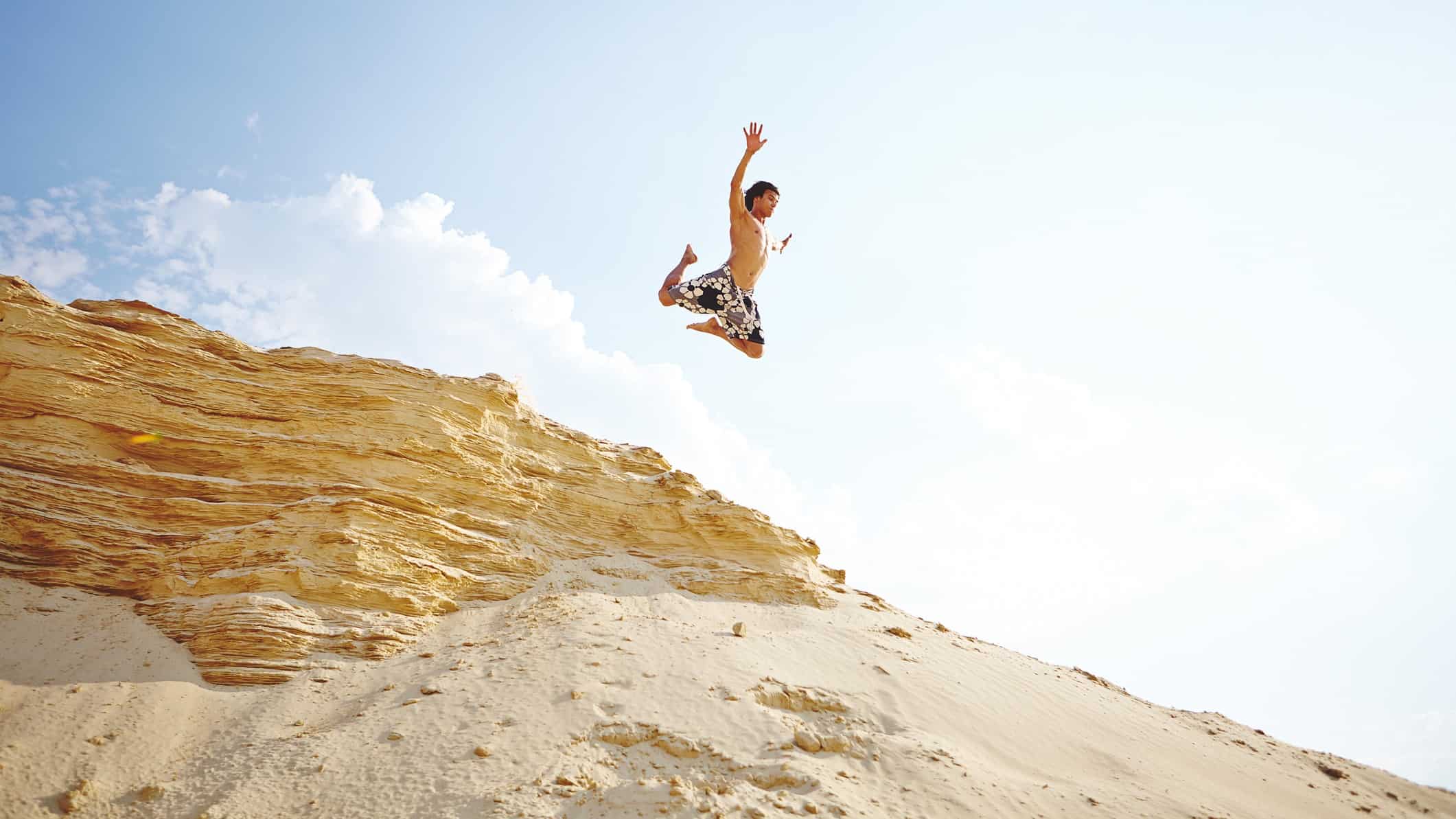 A man leaps high in the air over sand.