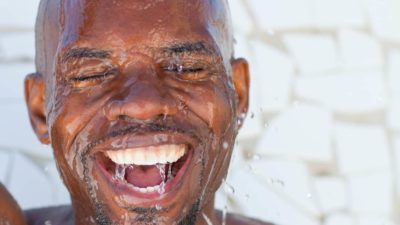 A man has a big smile on his face as he pours water over his head.