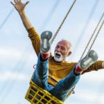 An older man throws his hands up in excitement as he rides a carnival swing high up in the air.