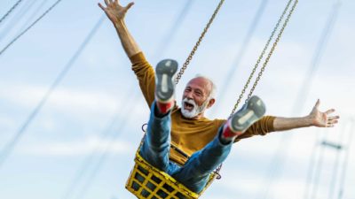 An older man throws his hands up in excitement as he rides a carnival swing high up in the air.