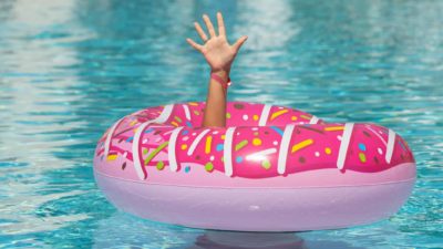 A hand reaches up through an inflatable doughnut pool toy asking for help.