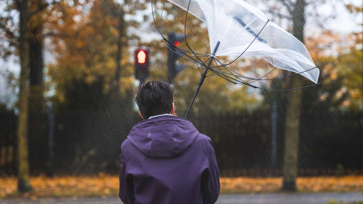A man's umbrella blows inside out in the wind and rain.