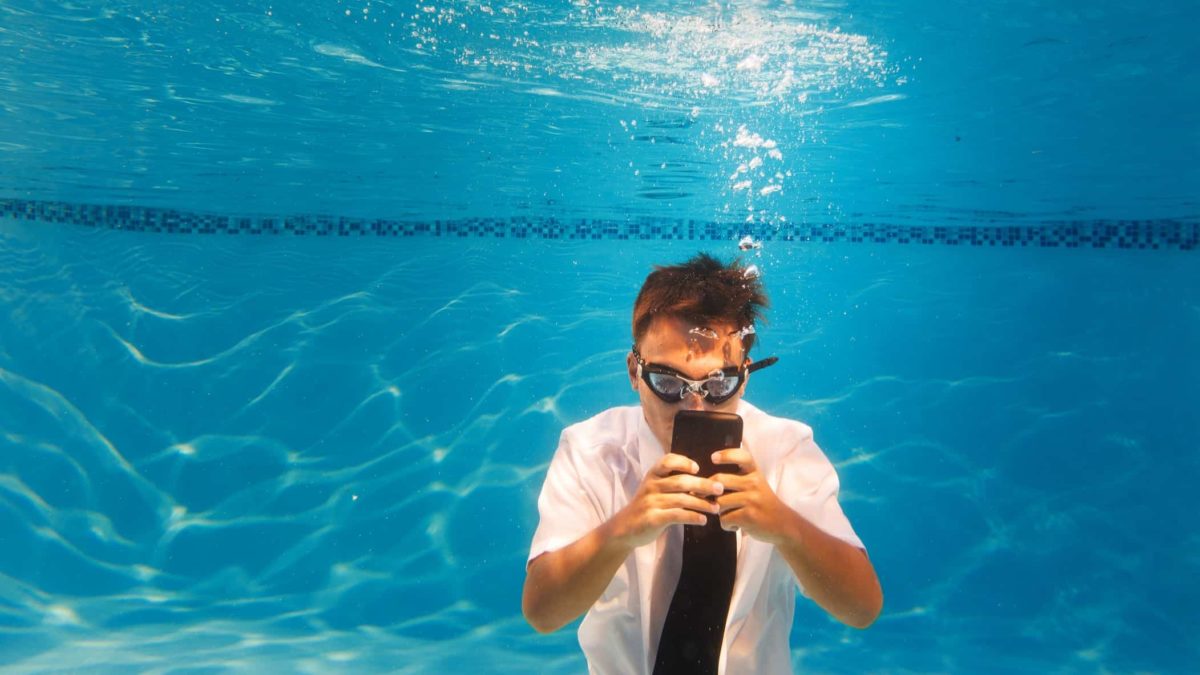A man in shirt and tie uses his mobile phone under water.