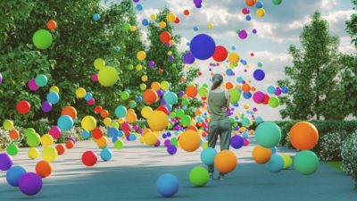 A woman standing on a path flanked by big green trees is surrounded by colourful balloons tumbling from the sky.