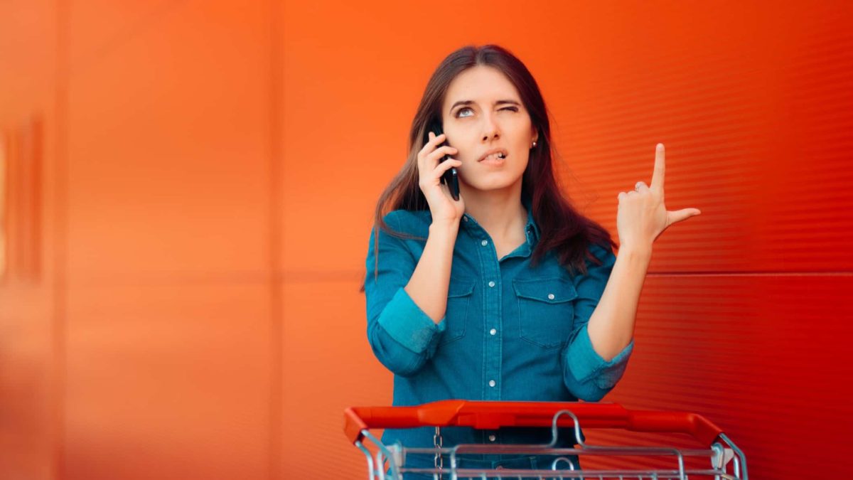 A woman standing with a shopping trolley is on the phone, thinking hard.