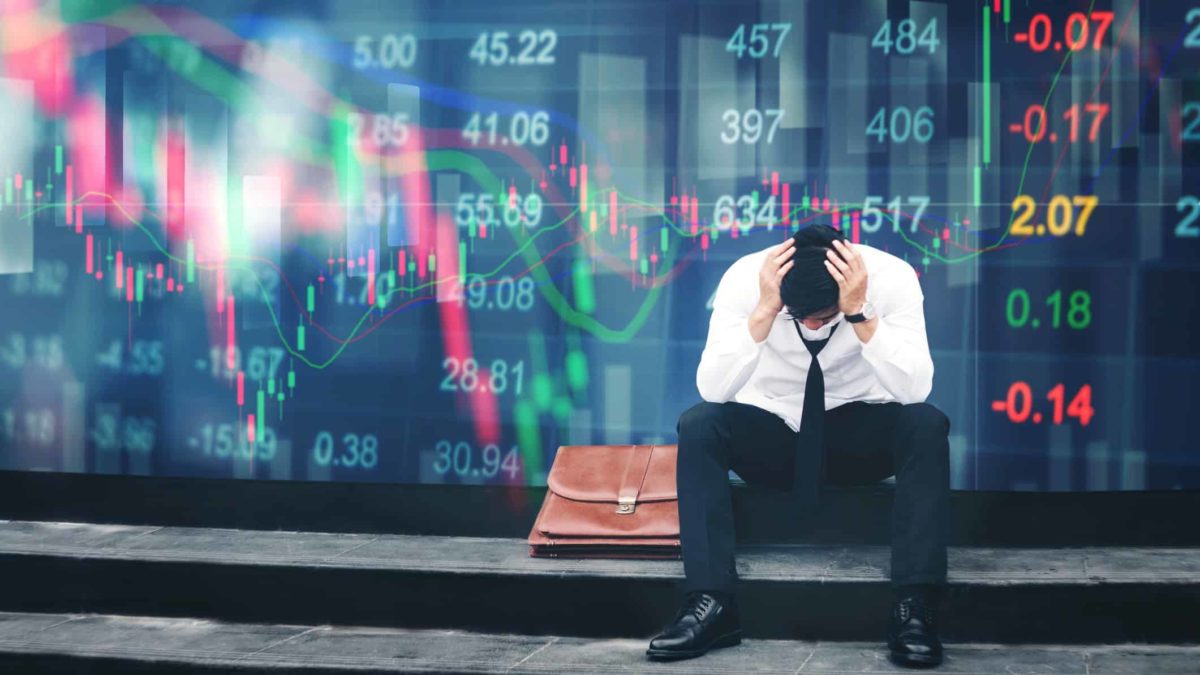 A stressed businessman in a suit shirt and trousers sits next to his briefcase with his head in his hands while the ASX boards behind him show BNPL shares crashing