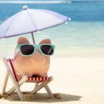A piggy bank sitting on the beach wearing sunglasses