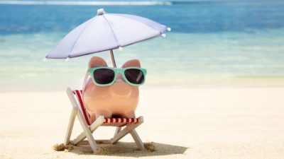 A piggy bank sitting on the beach wearing sunglasses