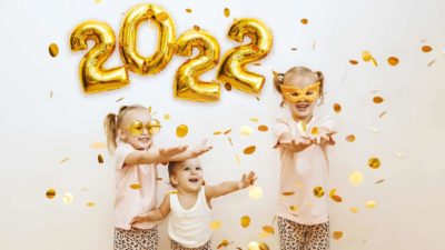 A group of children are showered with gold confetti against a backdrop of gold 2022 balloons.