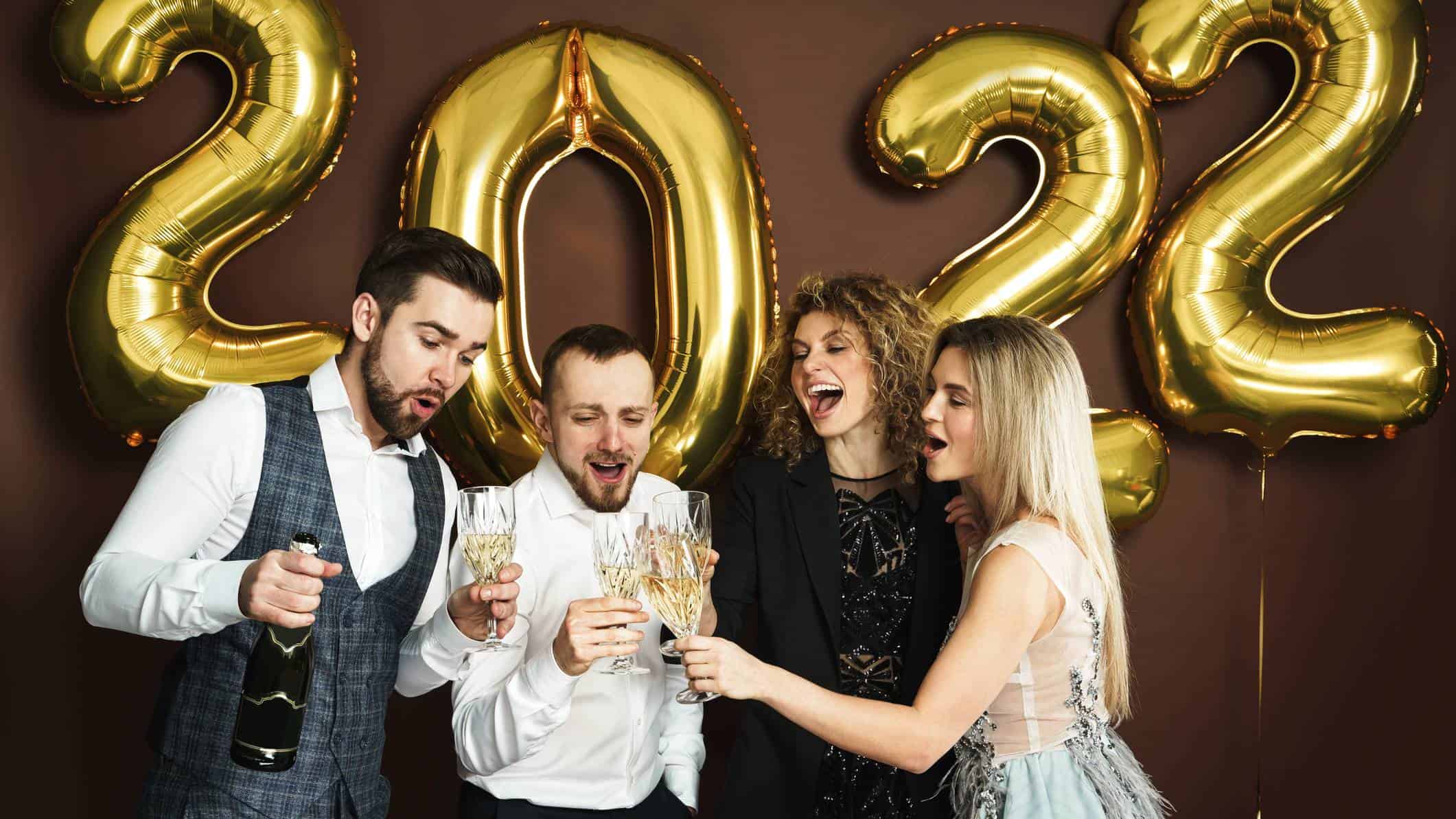 four people celebrate with champagne in front of gold 2022 balloons