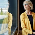 A woman wearing the black and yellow corporate colours of a leading bank gazes out the window in thought as she holds a tablet in her hands.