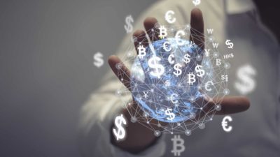 a close up of a hand is outstretched amid graphic images of currency and cyprtocurrency symbols seemingly floating around a sphere of light representing perhaps the globe.