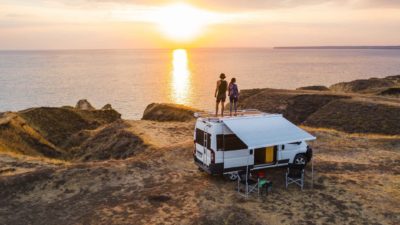A couple stand on a beachfront looking out over the ocean with their campervan in the foreground representing today's news of the Apollo share price surging