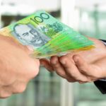 Close-up photo of a human hand with $100 bills offering the money to another human hand