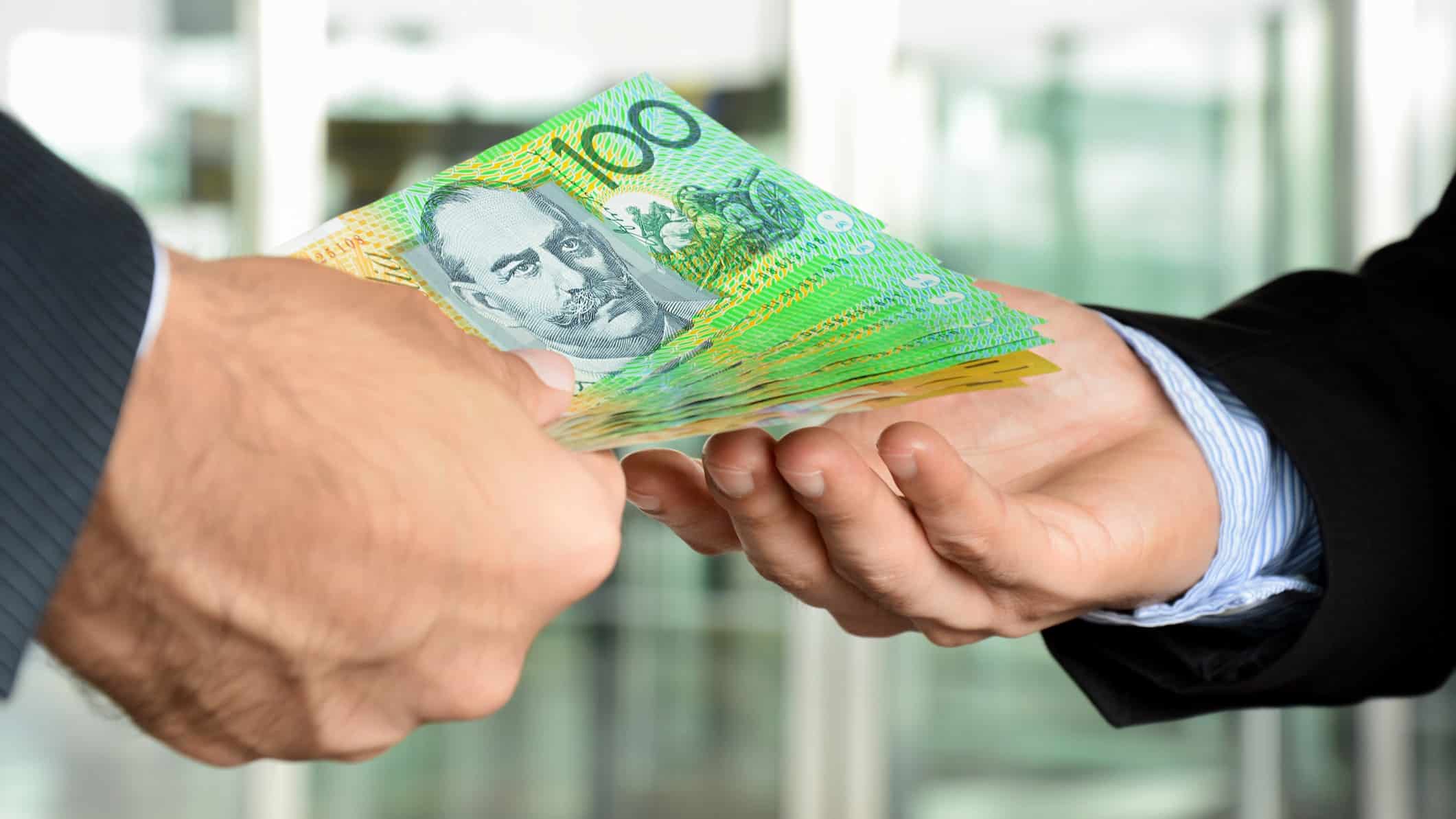 Close-up photo of a human hand with $100 bills offering the money to another human hand