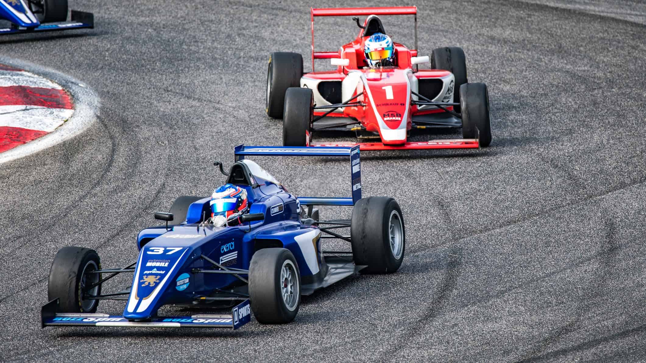 two racing cars battle to take first place on a formula one track with one tailing the the leader and looking to overtake the car.