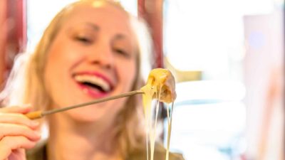 Woman holds up a piece of cheese fondue.