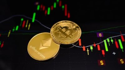 an image of a gold bitcoin and a gold ethereum coin side by side against a backdrop of a graph with reda and green bars representing rising and falling prices.