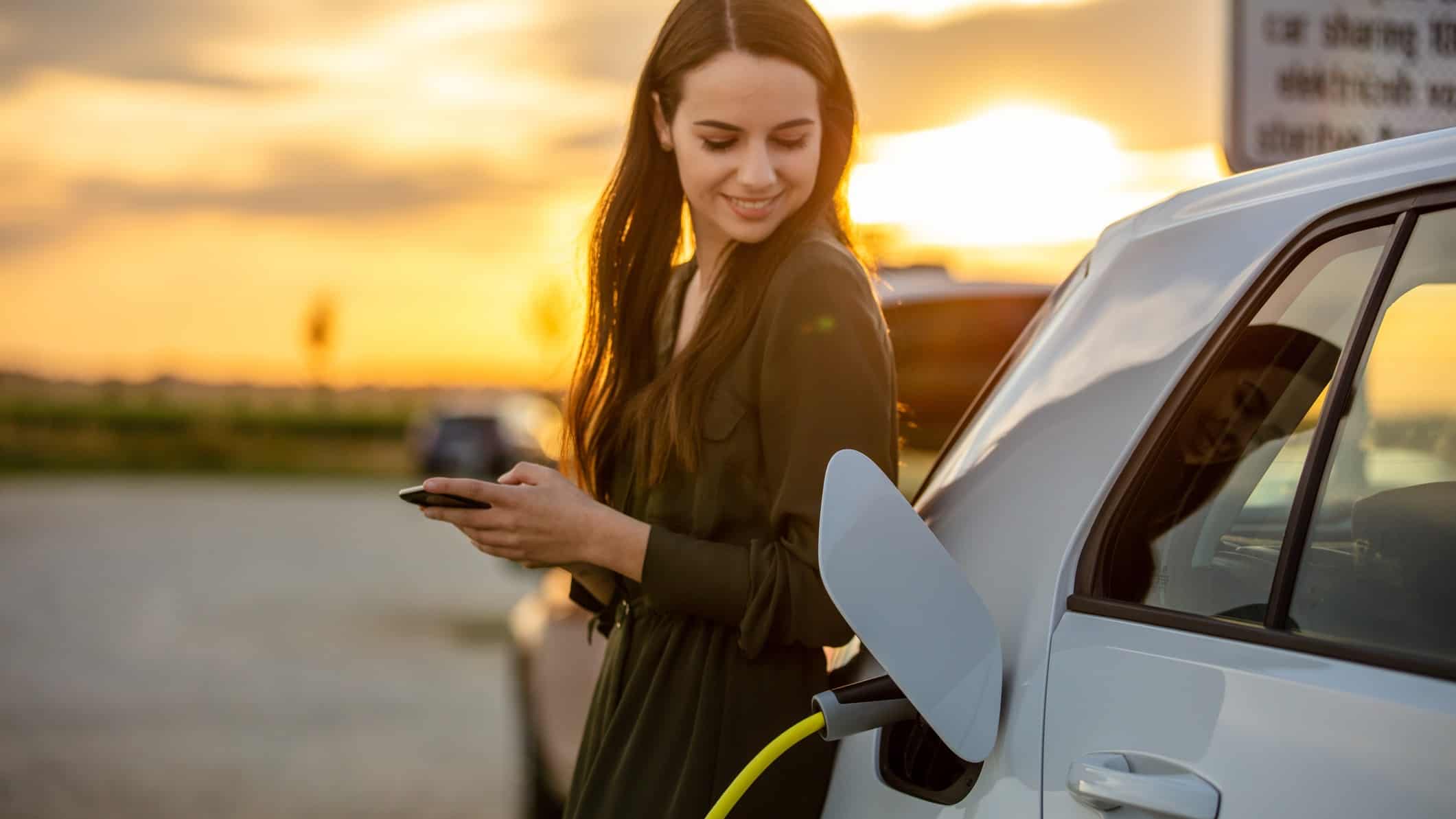 A woman smiles as she powers up her electric car using a Tritium fast charger