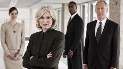 a panel of formidible business people stand in a group with serious looks on their faces as if in judgement of what's before them.
