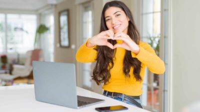 Young woman using computer laptop smiling in love showing heart symbol and shape with hands. as she switches from a big telco to Aussie Broadband which is capturing more market share