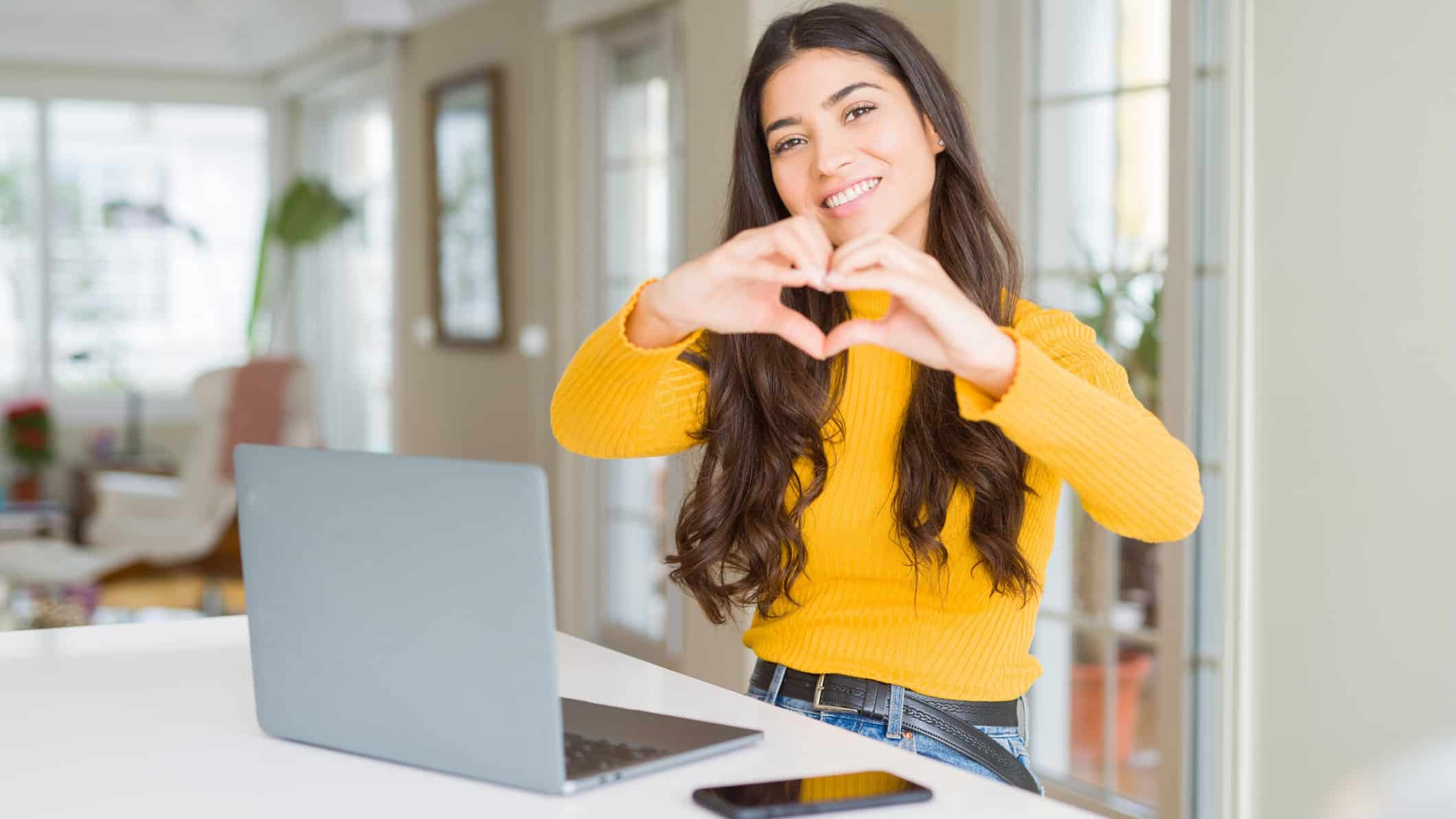 Young woman using computer laptop smiling in love showing heart symbol and shape with hands. as she switches from a big telco to Aussie Broadband which is capturing more market share
