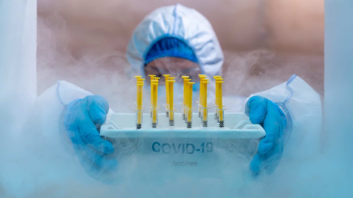 a medical person in full protective clothing holds a tray of Covid-19 vaccinations amid a haze caused by cold and ice.