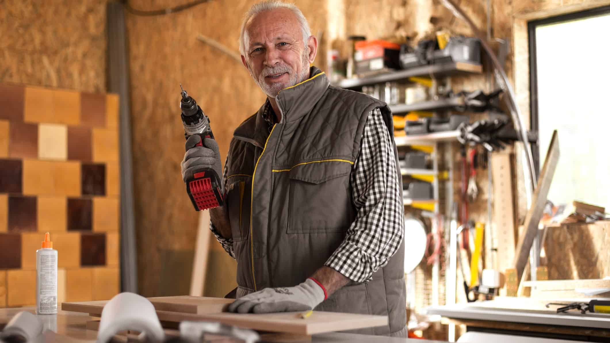 A man stands in his shed holding a cordless drill