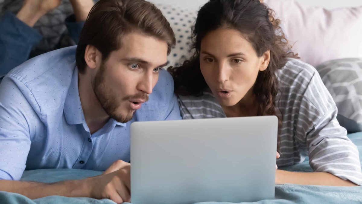 A man and a woman sit in front of a laptop looking fascinated and captivated.