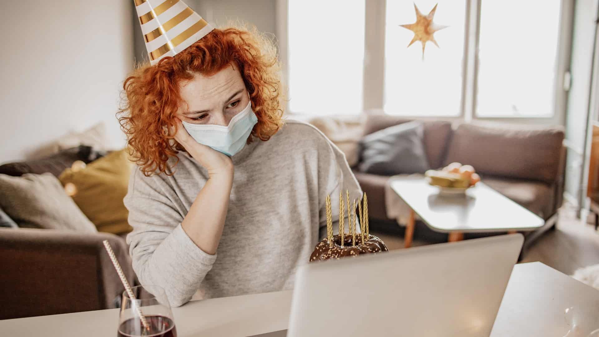 An investor sits at a table in front of her laptop with a party hat on her head and a cake next to her symbolising new year's eve but the 4DS Memory share price is plunging so she looks very disappointed and depressed