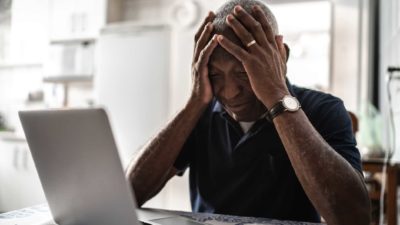 Man sits in front of laptop with head in hands.