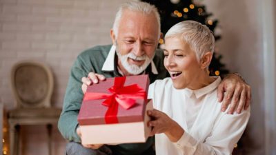 An older couple opening a gift near a christmas tree, showing a surprised emotion