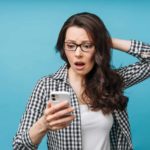 A woman looks distressed as she stares dramatically at her phone