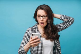 A woman looks distressed as she stares dramatically at her phone