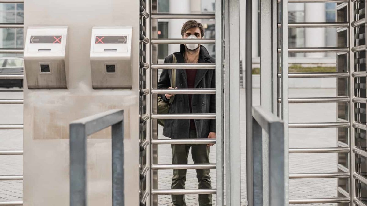 A man wearing a face mask is stuck behind some closed steel gates.
