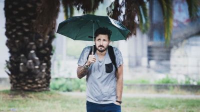 A man slumps his shoulders as he stands under his umbrella in the rain.