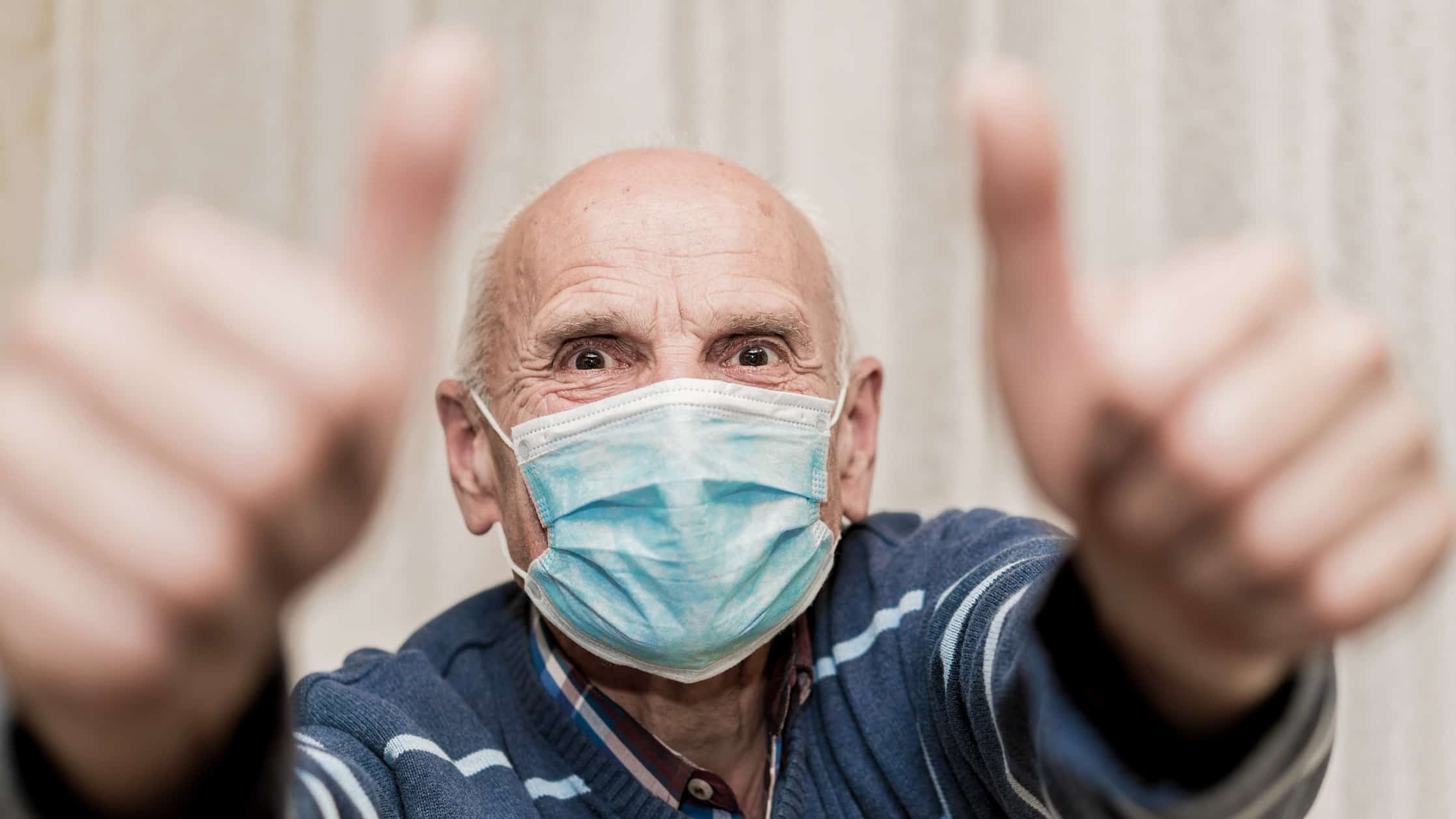 An elderly man wearing a face mask gives an excited double thumbs up.