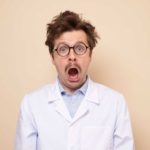 A man wearing a white coat and glasses is wide-mouthed in surprise.