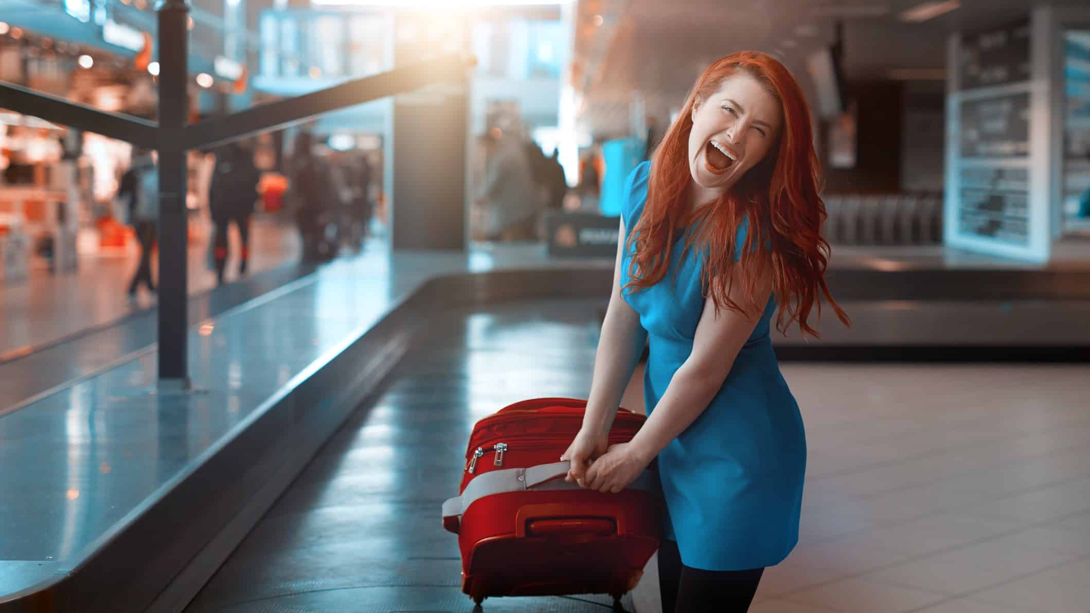 A woman is laughing with joy as she pulls her luggage off the conveyor belt at an airport.