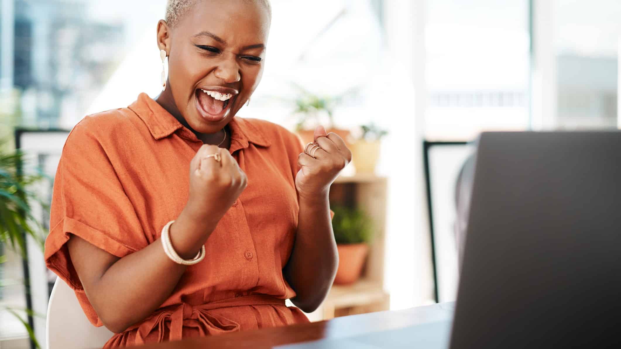 A young women pumps her fists in excitement after seeing some good news on her laptop regarding the NRW share price