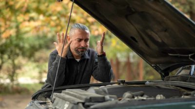 a man frustrated looking at the engine of his car