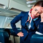 A female cabin crew member on a place looks like she has a headache.