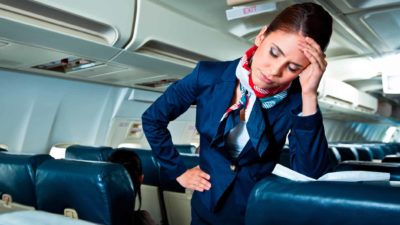 A female cabin crew member on a place looks like she has a headache.