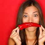 A woman holds a chilli in front of her mouth as an upside down smile.