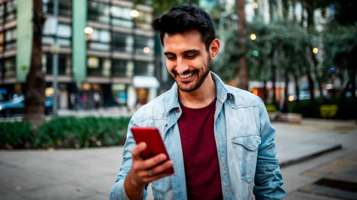 A man holding a mobile phone walks past some buildings